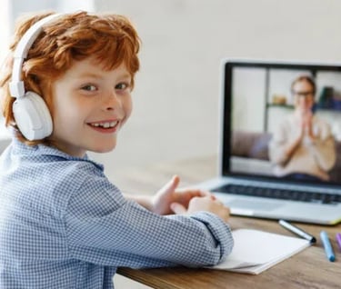 a young boy with headphones and a laptop, on the screen you can see his language tutor, both smiling