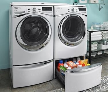 Front-loading washer and dryer in a laundry room with a storage drawer containing detergent and cleaning supplies underneath.
