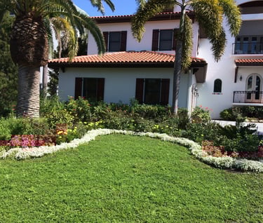 Stucco home with wrap around white flowers and another layer of colored flowers behind it.