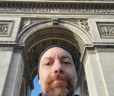 a man with a beard and a beard in front of a arc de trios