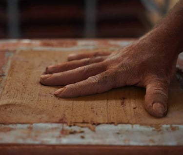 A potter's hand pressing and shaping a slab of raw terracotta clay in a ceramics studio.