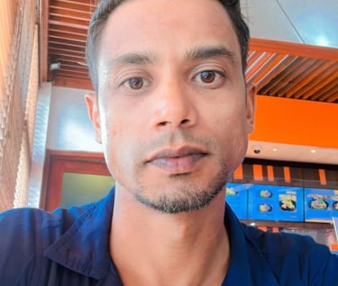 A man with styled dark hair and a blue shirt sitting in a modern cafe with wooden decor.