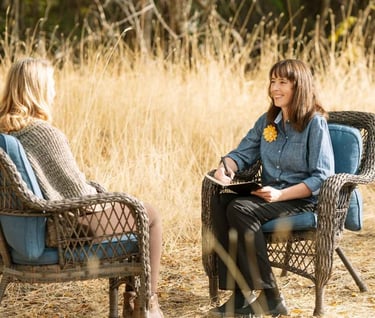 a woman sitting in a chair in a field listening to another women