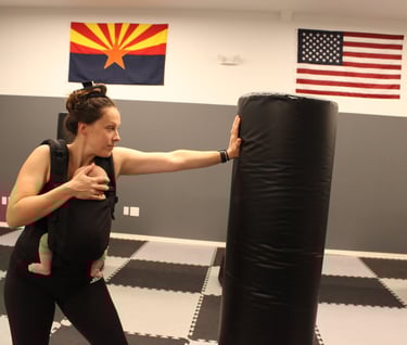 Instructor carrying her baby and striking a heavy bag 