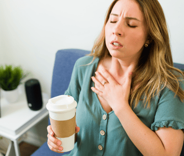 Uma mulher sentindo mal estar no peito, com um copo térmico de café na mão