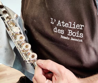 une vue de près du réparateur Romain Jacoulot avec son tablier de travail, tenant une flûte