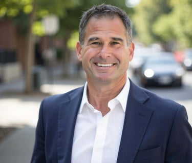 Professional portrait of a smiling middle-aged businessman in a navy blazer on a city street.