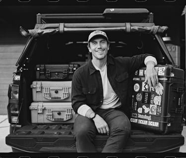 A smiling photographer sitting on a truck tailgate with outdoor gear and Pelican cases.
