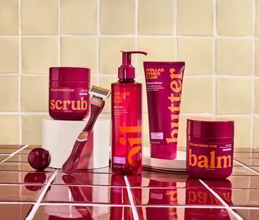 Dollar Shave Club men's grooming kit with razor, scrub, shave butter, oil, and balm on a tiled background.