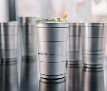 A chilled recyclable aluminum cup filled with an iced cocktail and fresh mint garnish.