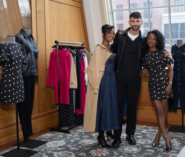 Three people posing in a fashion showroom with designer clothing displays and polka dot dresses.