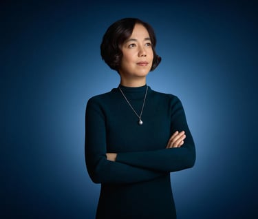 Professional portrait of a confident woman with arms crossed, wearing a dark sweater and pearl necklace.