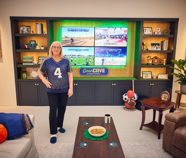 Senior woman standing in a sports-themed fan cave with multi-screen TV displaying live games.