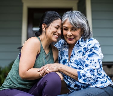 Smiling senior Hispanic mother and adult daughter hugging and sharing a tender moment together outdoors.