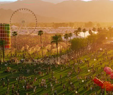 Sunset at Coachella music festival with crowds, Ferris wheel, and palm trees in the desert.