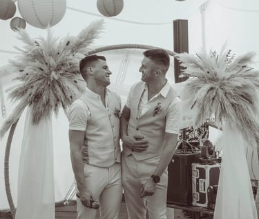 Smiling grooms celebrating a modern boho wedding ceremony under a pampas grass arch.
