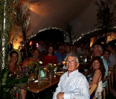 Guests enjoying an outdoor dinner party under a decorated tent with string lights and greenery.