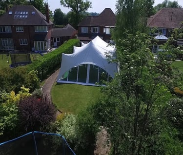 White garden party marquee tent set up in a lush residential backyard for an outdoor event.
