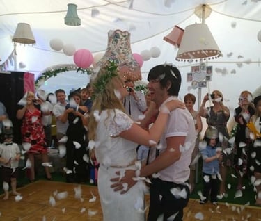 A happy bride and groom celebrate their first dance under white confetti in a decorated wedding marquee.