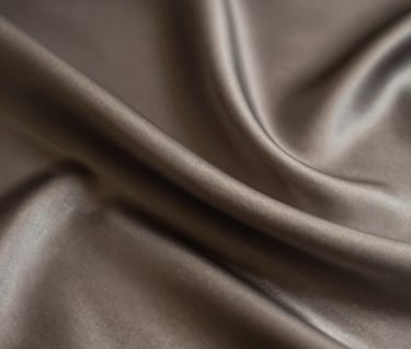 A minimalist composition of fine silk fabric draping in the dark, with soft light catching the edges in beige and charcoal tones, reflecting luxury and distinction.