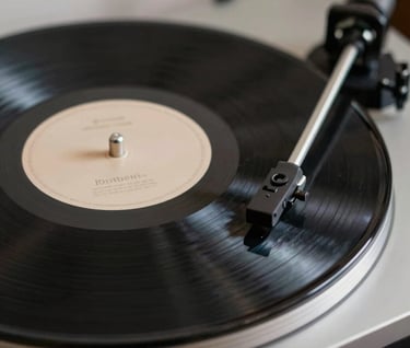Macro shot of a high-fidelity vinyl record player. The spinning black record reflects the soft lights of a refined studio. A touch of sand color (#DDCBC0) is visible in the record label's elegant typography.