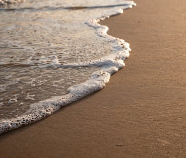 Abstract close-up of soft waves washing over sand, captured in warm morning light, cinematic textures and peaceful mood.