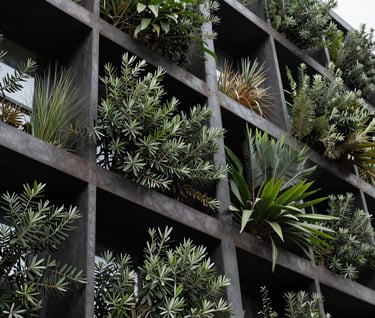 A detail shot of a biophilic architectural facade. Rich olive green plants are integrated into a dark charcoal metal structure. The lighting is crisp and clear, emphasizing the intersection of the organic and the built environment.