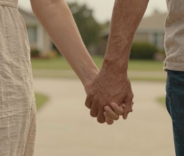 A cinematic detail shot of two parents' hands entwined while walking, shallow depth of field, North American / US suburban garden setting, warm golden light and soft sand textures.