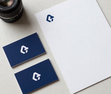 A top-down view of corporate identity materials, including business cards and a letterhead, featuring a minimalist logo in navy blue, arranged neatly on an off-white textured surface.