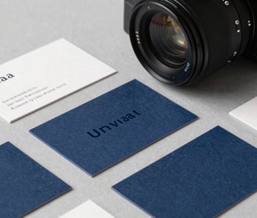 High-end photography of a physical brand identity presentation, featuring minimalist business cards with dark navy typography and a slate blue texture, arranged neatly on a light gray surface in a modern North American setting.