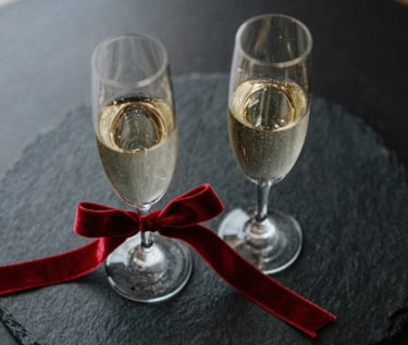 Top-down view of two champagne glasses on a black slate table, with a red velvet ribbon tied around one stem, North American / US luxury wedding style.