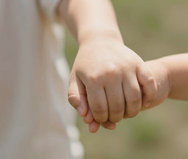 A detailed close-up shot of a small child's hand holding a parent's hand. Soft focus on the background. Warm, natural skin tones and sun-drenched lighting.