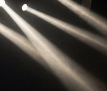 A blurry, artistic shot of stage lights through a hazy rock club atmosphere. High contrast with deep black and soft off-white streaks.