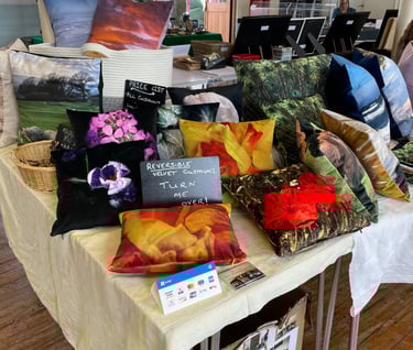 a selection of various handmade velvet cushions with nature photo prints on a craft stall display