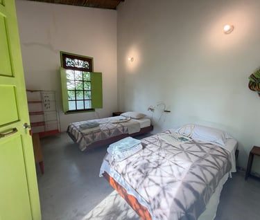 Rustic twin bedroom with green shutters, white walls, and cozy beds in a boutique guest house.