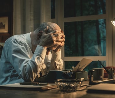 Fotografía de un hombre frente a una máquina de escribir, cogiéndose la cabeza perturbado.