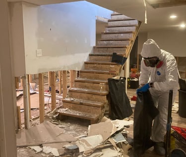 Biohazard hazmat man in white suit with blue gloved picking up trash in a unfinished basement