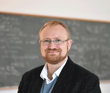 a man in a suit and glasses standing in front of a chalkboard
