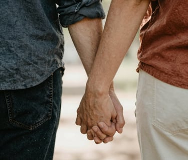 A candid, close-up photograph of a couple's hands intertwined, wearing casual North American attire. Sunlight filters through the scene, creating a warm, hazy atmosphere. Lifestyle photography style, focusing on real-world textures and charcoal and terracotta accents.