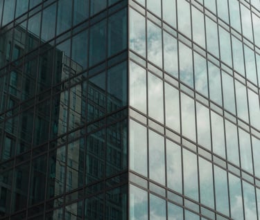 Abstract architectural photography of a glass skyscraper corner. Reflections of the sky in deep muted teal and soft sage are visible on the surface. The lines are sharp and perfectly aligned, emphasizing a clean, modern aesthetic.