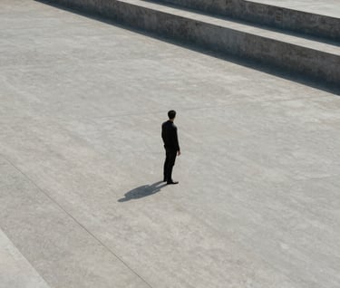 A cinematic, wide-angle photograph of a lone figure in dark clothing standing in a vast, open concrete plaza with strong geometric lines, Global / Contemporary Art.