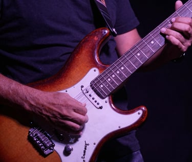 A close-up artistic photography shot of hands playing a vintage electric guitar, South American / Venezuelan context, deep shadows with dusty purple and rose lighting, reflecting a rock and soul vibe.