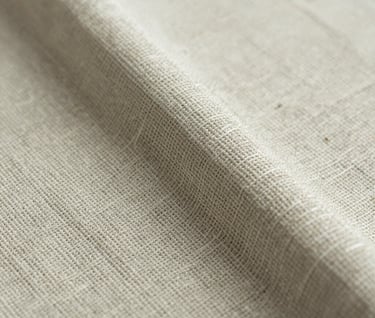 A macro photograph focused on the texture of a hand-woven fabric. The colors are muted sage and ivory, showing the delicate interplay of fibers and the organic imperfections typical of high-end, artisan textile production.