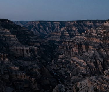 A wide cinematic landscape still from a completed feature film, capturing a vast North American valley at dusk, sophisticated deep charcoal black and muted blue gray color palette.