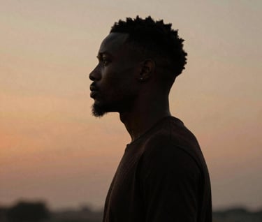 An artistic silhouette of P.E.P YLS against a warm #8D765D sunset backdrop, highlighting his profile. The image has a grainy, film-like quality that adds artistic depth, reflecting the soulful nature of his music and his Nigerian-American heritage.