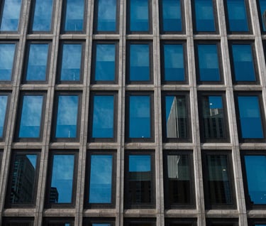 Modern urban facade with repeating geometric windows reflecting a cerulean blue sky, North American city.