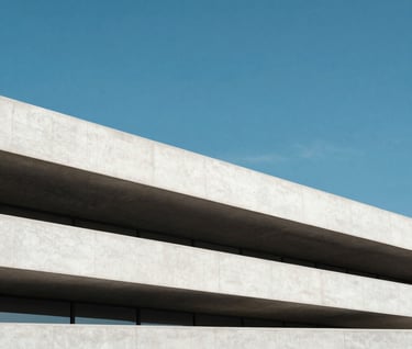 An outdoor photograph of a minimalist concrete structure in a North American city. The white concrete forms sharp horizontal lines against a vibrant cerulean blue sky. The lighting is crisp, highlighting the sophisticated and clean aesthetic of the project.