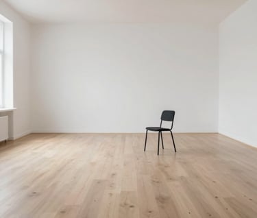 A wide, cinematic shot of an empty minimalist studio space with white walls and a light wood floor. A single, refined black (#1A1A1A) chair stands in the distance. Soft light pours in from an invisible source, highlighting the 'space' and 'air' of the brand.