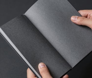 Close-up of hands holding a thick, matte-finished brand manual with silver foil details, shot in a desaturated, high-craft aesthetic against a deep charcoal background.