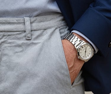 Detail shot of high-quality fabric texture and a silver watch on a man's wrist, sharp focus, elegant and professional lighting, aesthetic palette of light gray and dark blue.